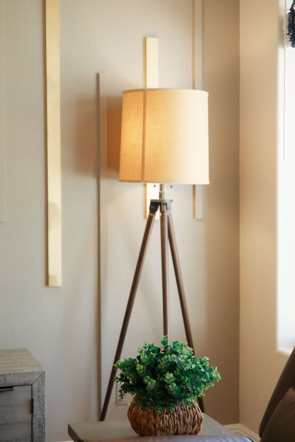 A close detail of a linen-shaded tripod floor lamp and a small potted plant in the living room.