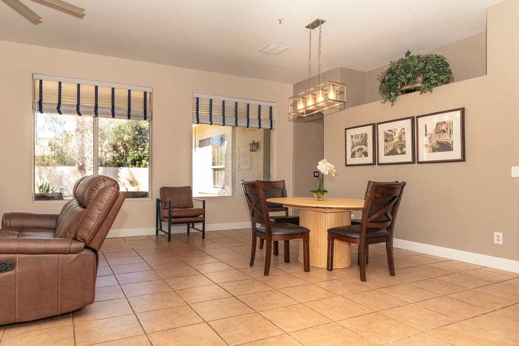 A dining corner off the living room: a round timber table with four dark wood chairs beneath a brass pendant light and framed prints.