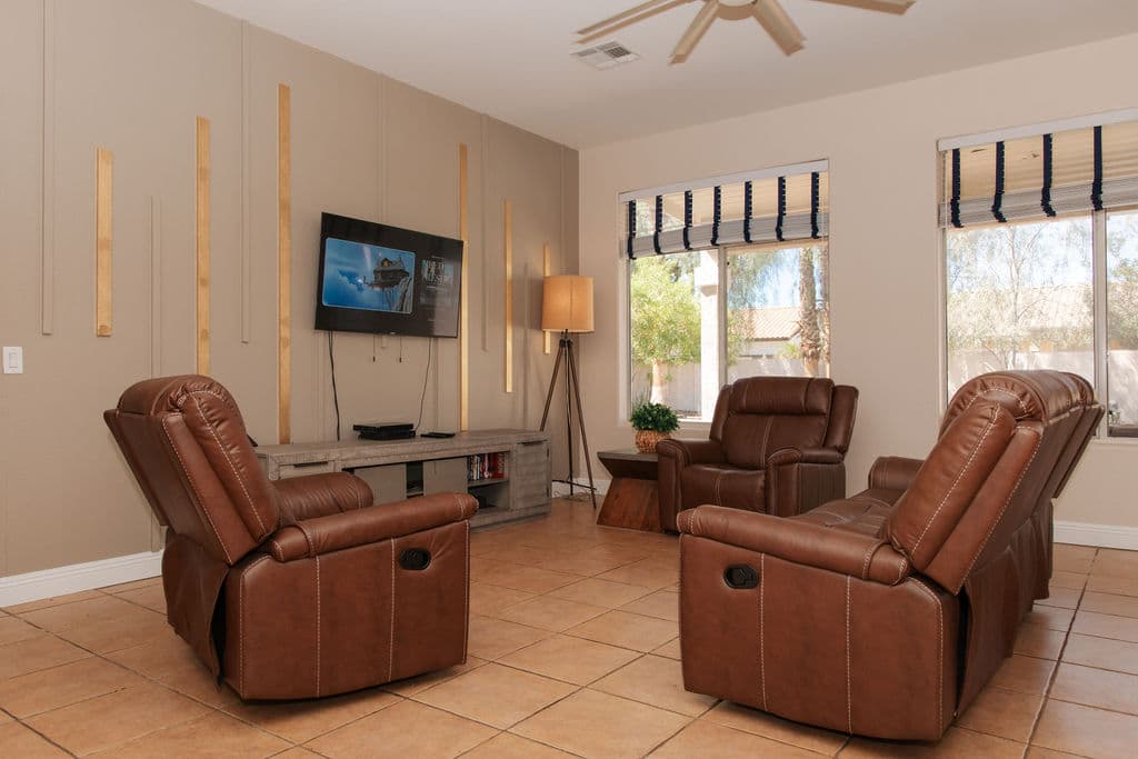 The Liora living room, with leather recliners arranged around a television wall, tall windows and warm natural light.